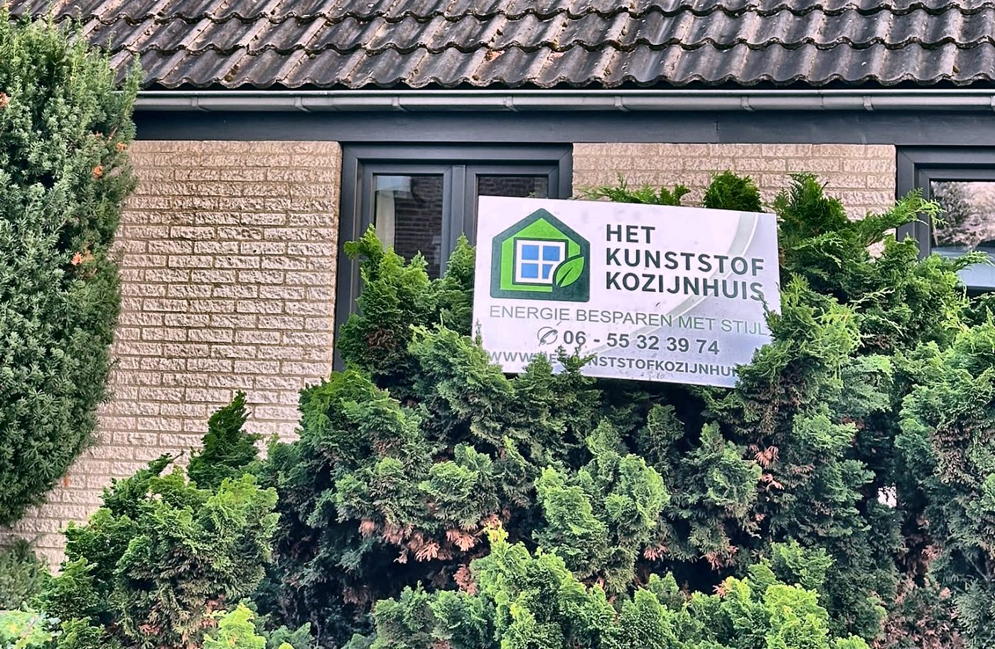 Nieuwe antracietgrijze kunststof kozijnen in de voorgevel, met het bord van Het Kunststof Kozijnhuis in de tuin